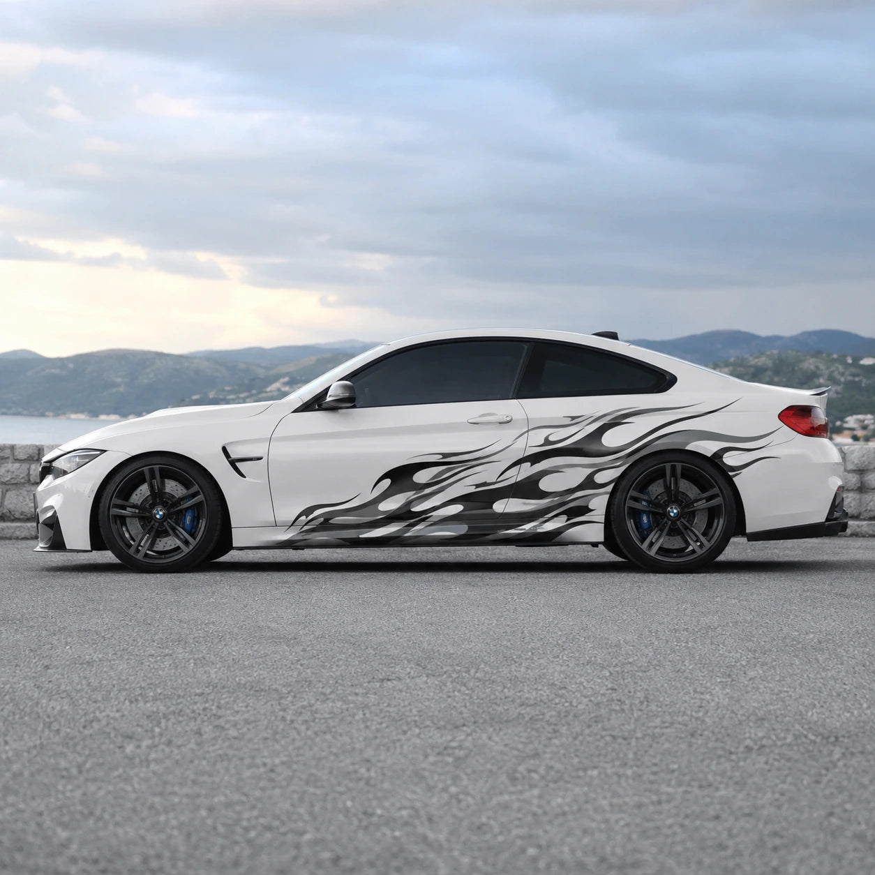 White BMW M4 with black flame side graphic decal parked by coastal road – full side profile