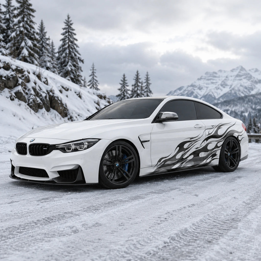 Black flame vinyl car side decal on white BMW M4 – front 3/4 view in snowy mountain setting