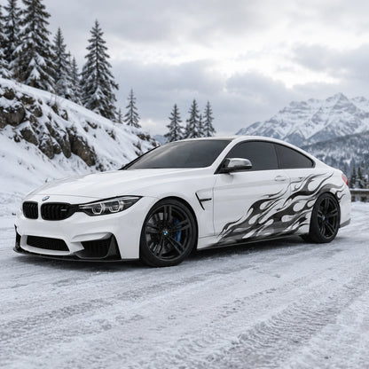 Black flame vinyl car side decal on white BMW M4 – front 3/4 view in snowy mountain setting