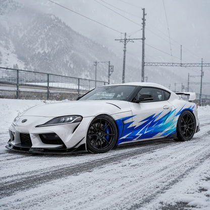 White Toyota Supra GR with blue lightning car side decal – front 3/4 view on snowy mountain road with overcast sky
