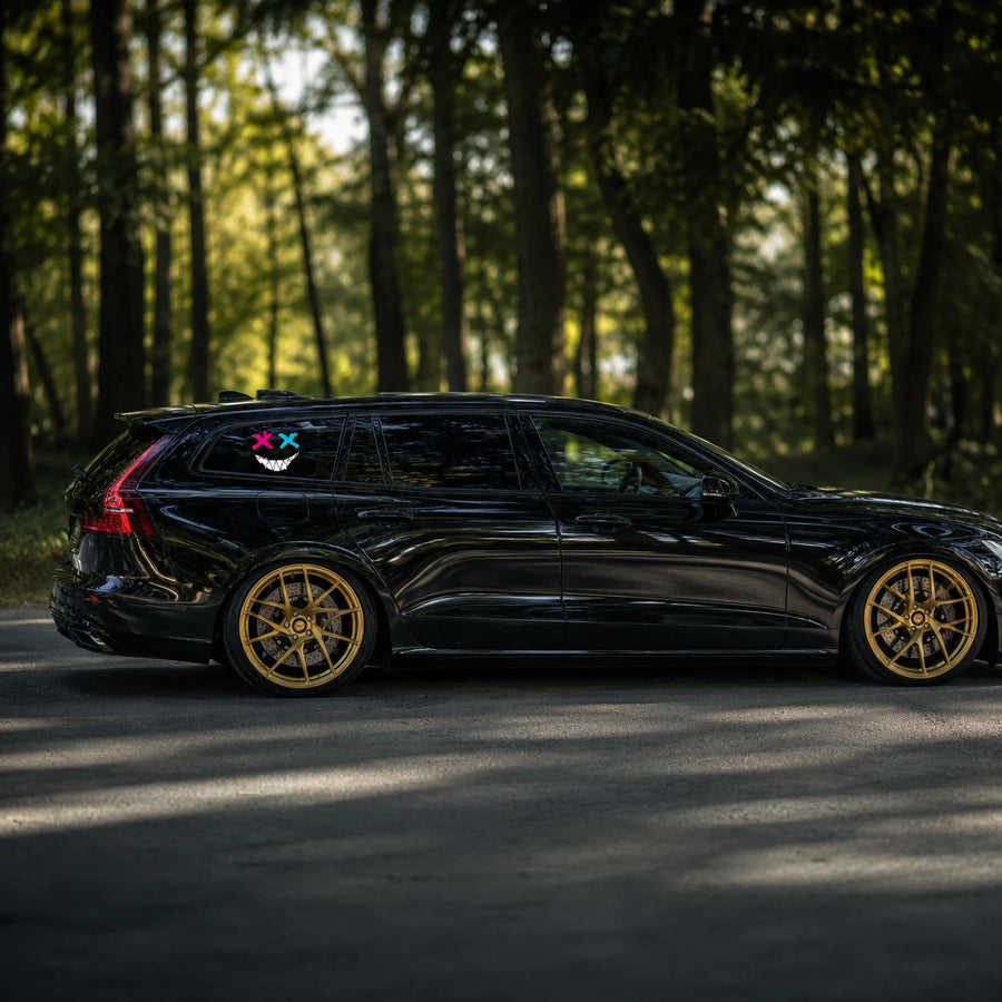 Evil XX smiley face vinyl decal installed on black Volvo V60 wagon rear quarter window full side view in forest road