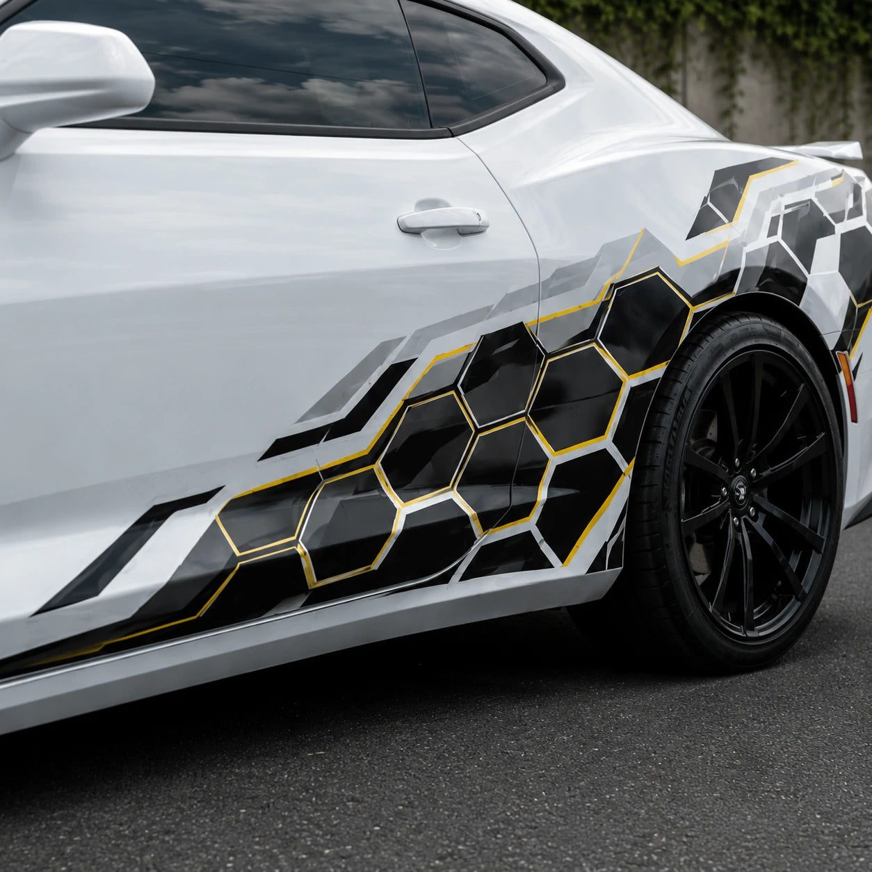 Close-up of black and gold honeycomb hex vinyl decal on white car door panel – detailed geometric pattern view