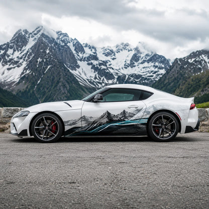 White Toyota Supra GR with mountain landscape side decal – full side profile on alpine mountain road with rocky peaks backdrop