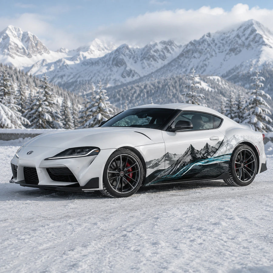 White Toyota Supra GR with mountain landscape car side decal – front 3/4 view in snowy alpine forest with mountain peaks