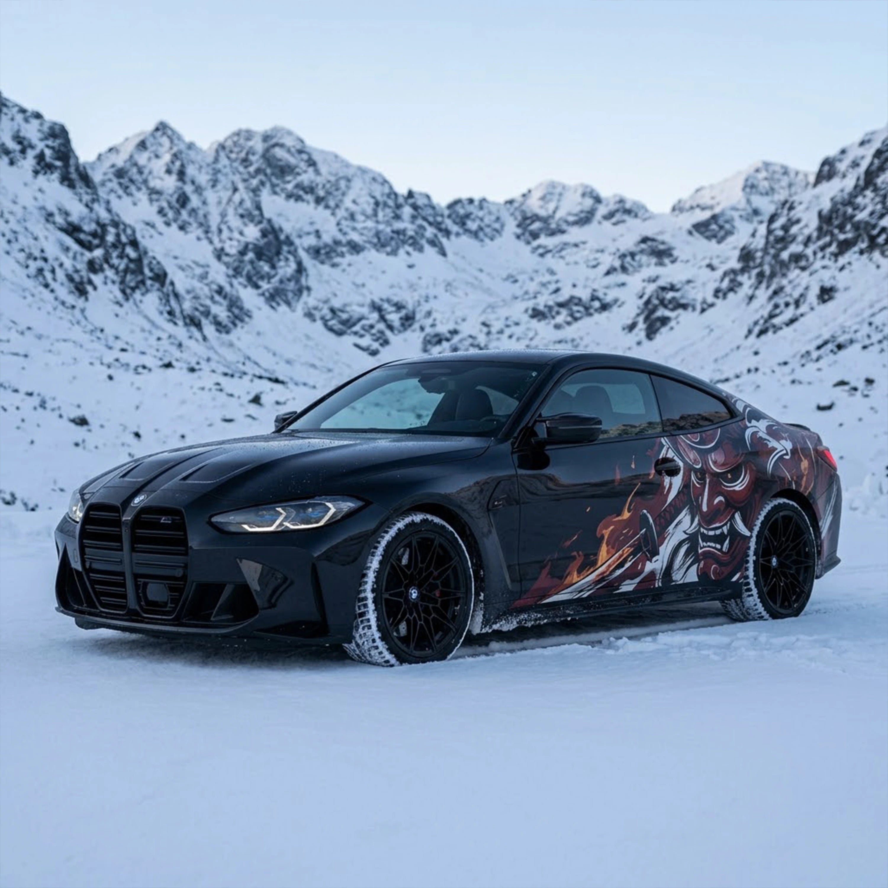 Black BMW M4 with Oni demon car side decal – front 3/4 view in snowy alpine mountain landscape