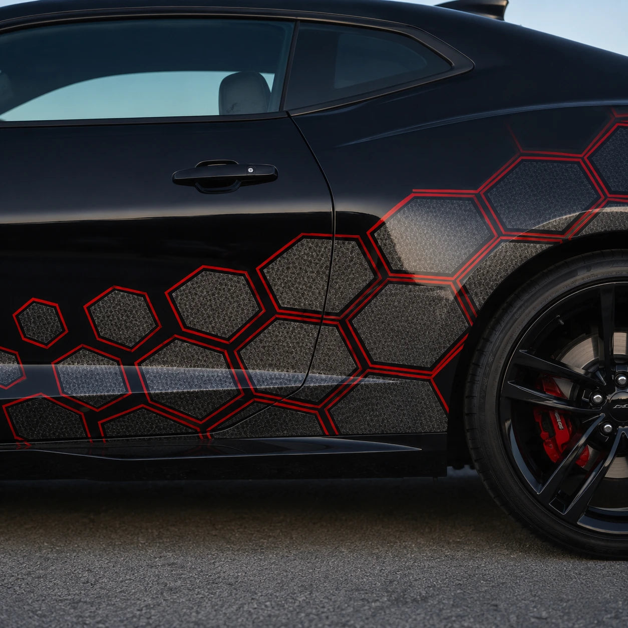 Close-up of black and red honeycomb hexagon vinyl decal on black car door and rear quarter panel – detailed pattern view