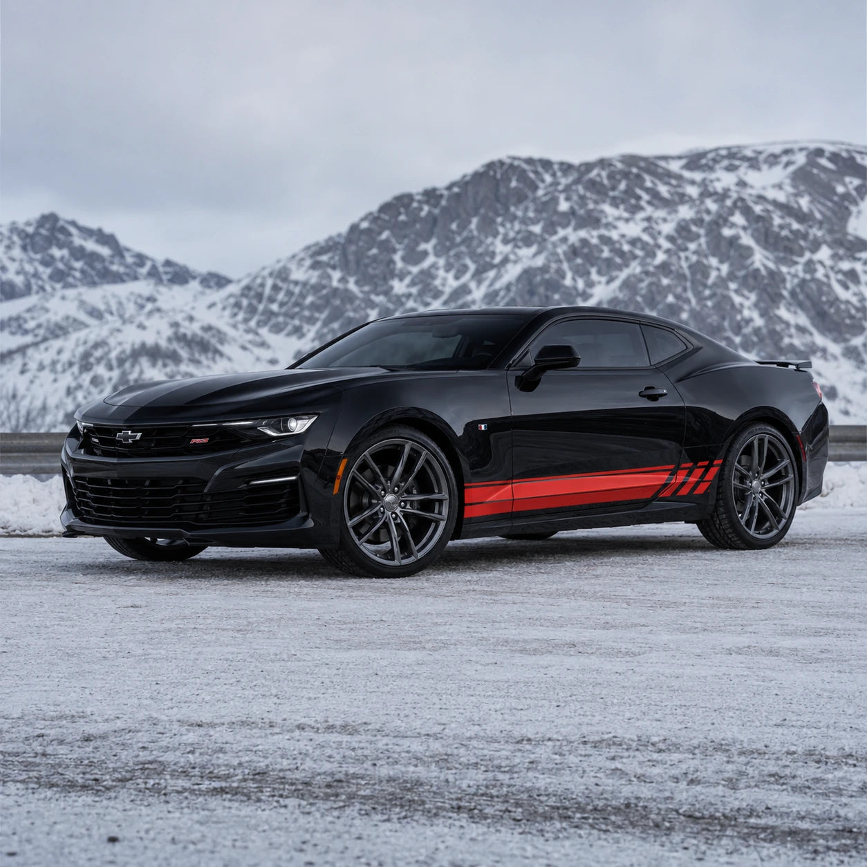 Black Chevrolet Camaro RS with red racing stripe side decal – front 3/4 view in snowy mountain landscape