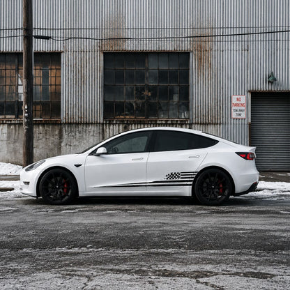 Tesla Model 3 with black distressed American flag side decal parked in front of industrial warehouse in winter