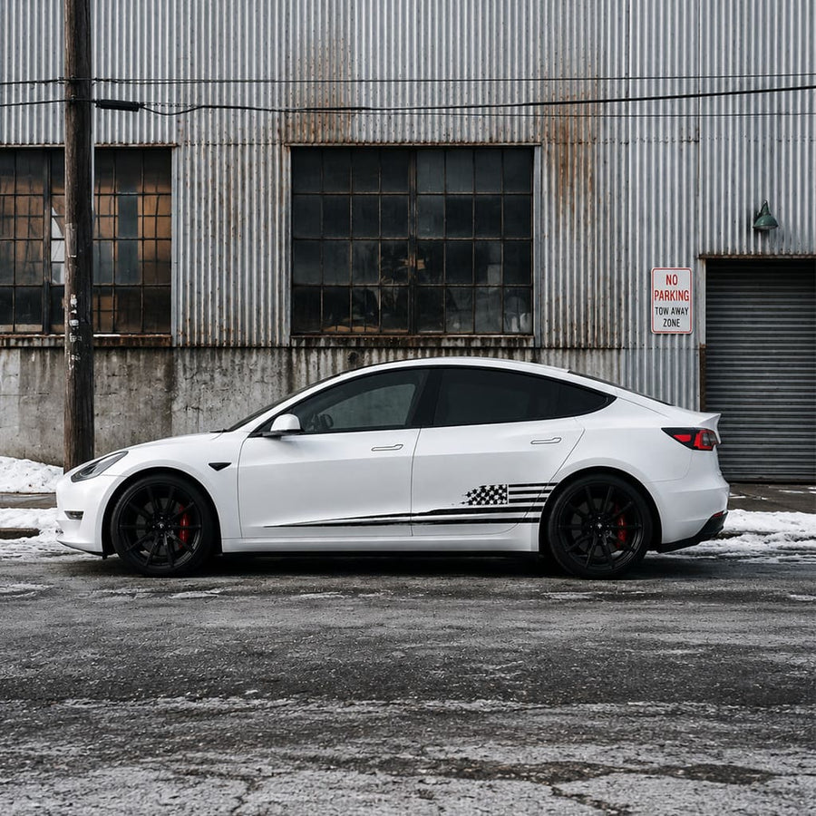 Tesla Model 3 with black distressed American flag side decal parked in front of industrial warehouse in winter