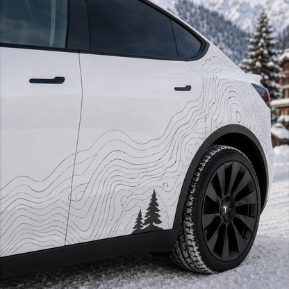 Tesla Model Y topographic contour line decal close-up rear door panel pine tree silhouette detail snowy mountain chalet background