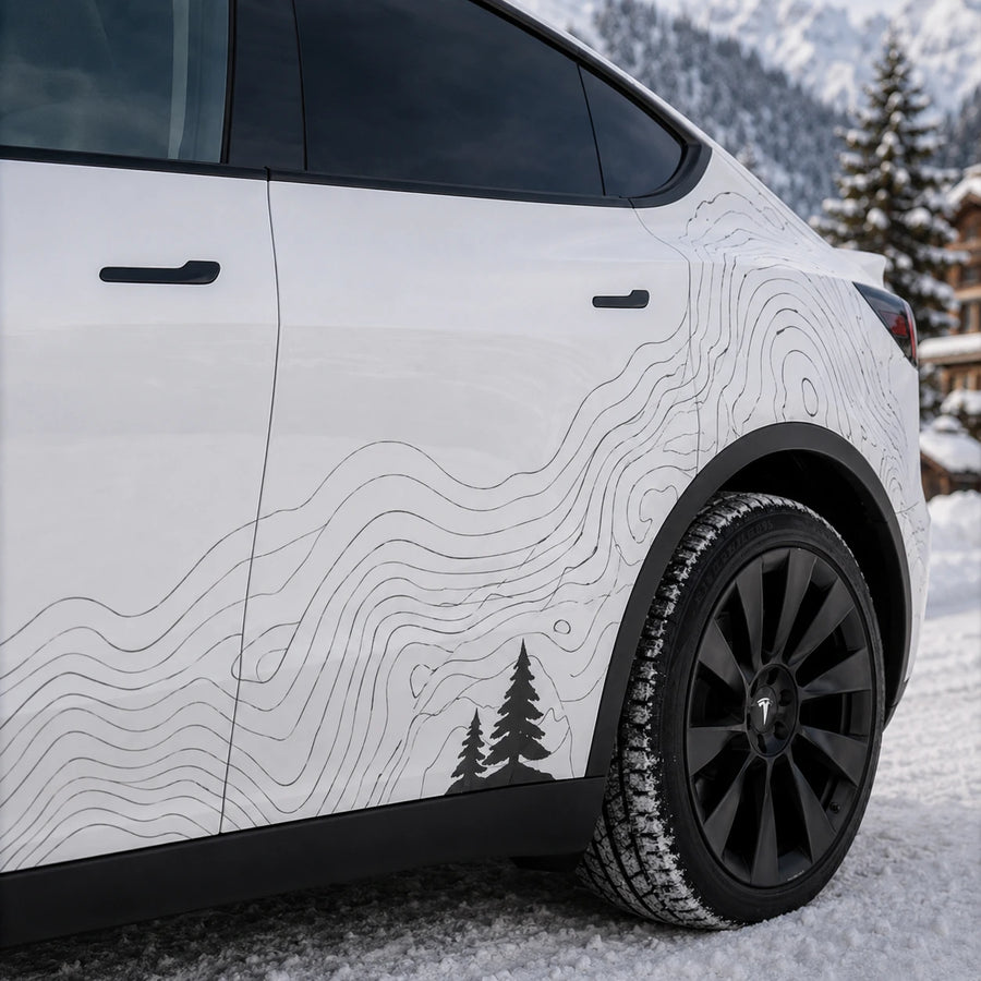 Tesla Model Y topographic contour line decal close-up rear door panel pine tree silhouette detail snowy mountain chalet background