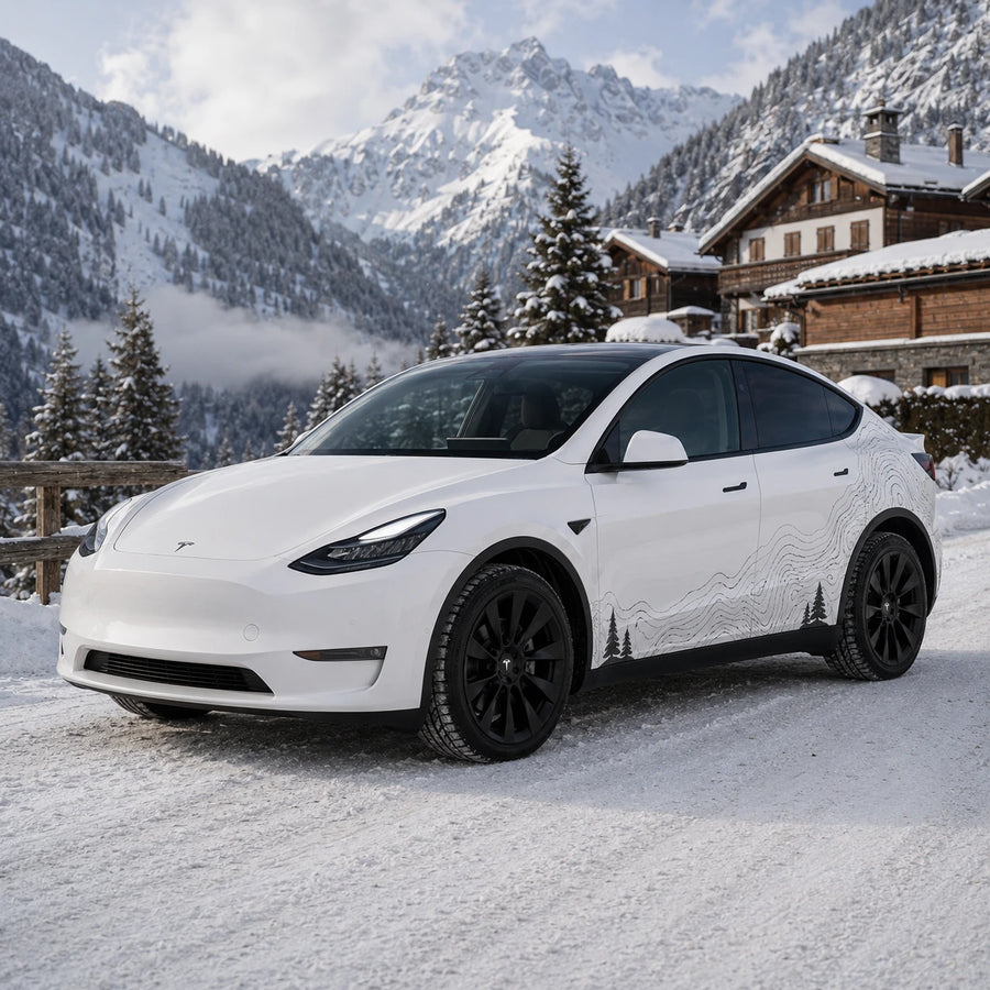 Tesla Model Y topographic mountain pine tree decal front three-quarter view snowy alpine chalet mountain village winter background