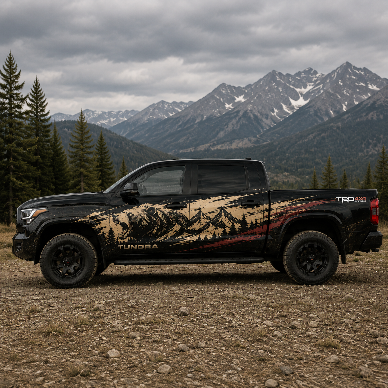 Driver side view of black Toyota Tundra TRD 4x4 with roaring bear mountain wilderness decal in tan and black, parked on rocky terrain with alpine backdrop